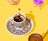 A persons hand is placing a teacup on a large golden stand with Dr Honeybrews Juicy Fortunes written on it with a liquid pouring into the cup from a spout