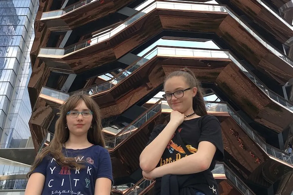 Two people are posing in front of the Vessel structure at Hudson Yards in New York City