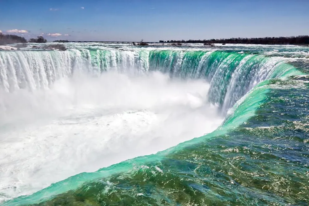 The image shows a majestic view of cascading water over the crest of Niagara Falls against a blue sky with scattered clouds