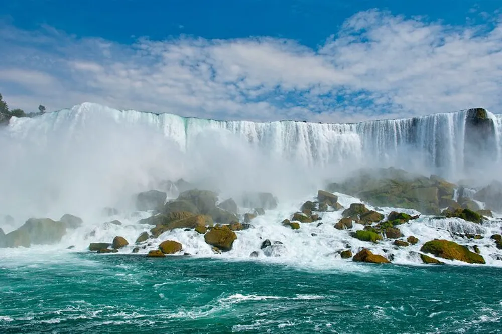 The image shows the powerful and scenic Niagara Falls with cascading water and mist rising above the turbulent waters and rocky base