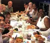 A diverse group of people is smiling at the camera while enjoying a meal together at a long table