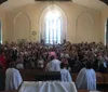The image shows a congregation of people inside a church applauding with some individuals standing at the front of the church dressed in white robes