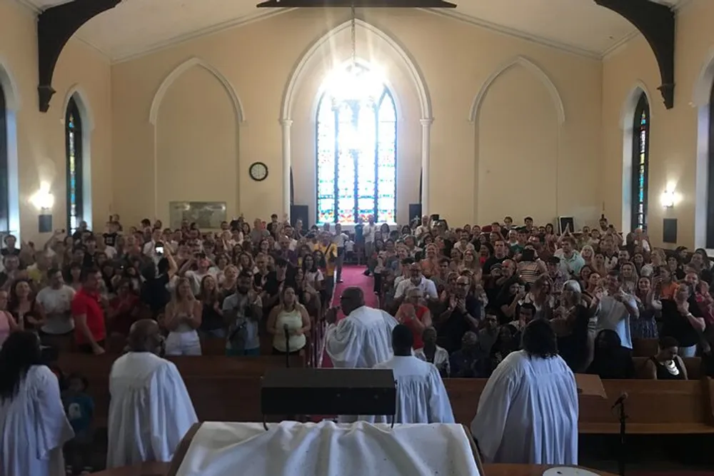 The image shows a congregation of people inside a church applauding with some individuals standing at the front of the church dressed in white robes