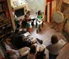 A group of people is congregated in a cozy room filled with books and artwork engaged in what appears to be a creative workshop or gathering
