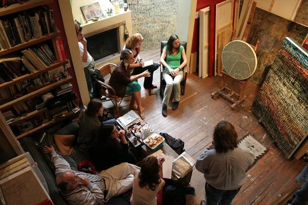 A group of people is congregated in a cozy room filled with books and artwork engaged in what appears to be a creative workshop or gathering