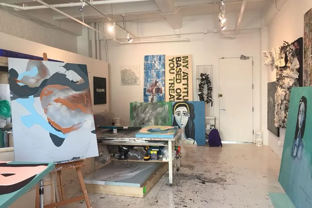 An art studio with various paintings on easels and hung on the walls showcasing different styles and a creative work environment splattered with paint