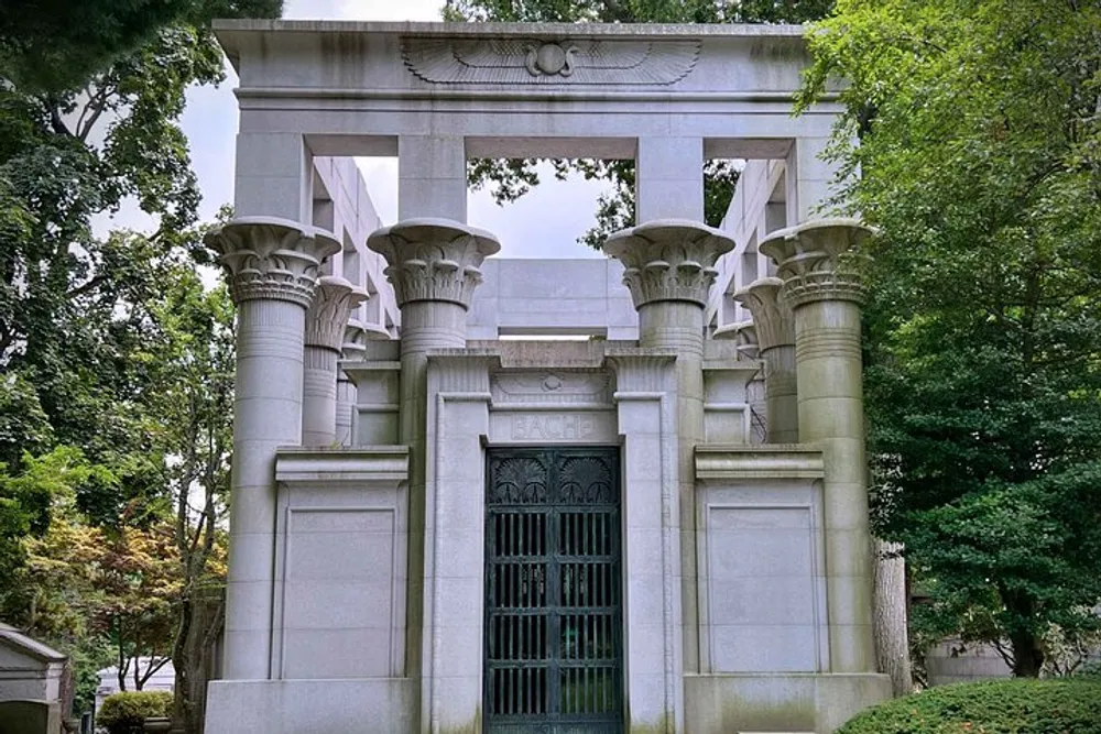 The image shows an ornate classical-style mausoleum with large columns and an intricate metal gate nestled in a serene tree-dotted landscape