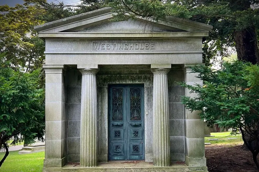 The image shows a stately mausoleum with the name WESTINGHOUSE engraved above the ornate metal doors surrounded by greenery in what appears to be a peaceful cemetery setting