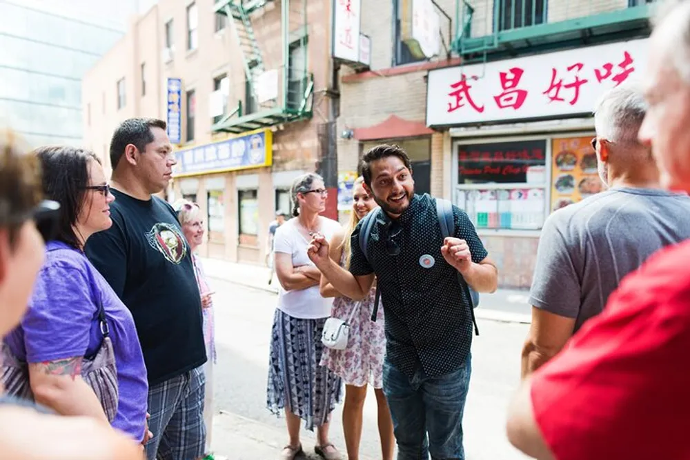 A joyful man gestures excitedly while telling a story to a group of attentive people on an urban street flanked by businesses with Chinese signage