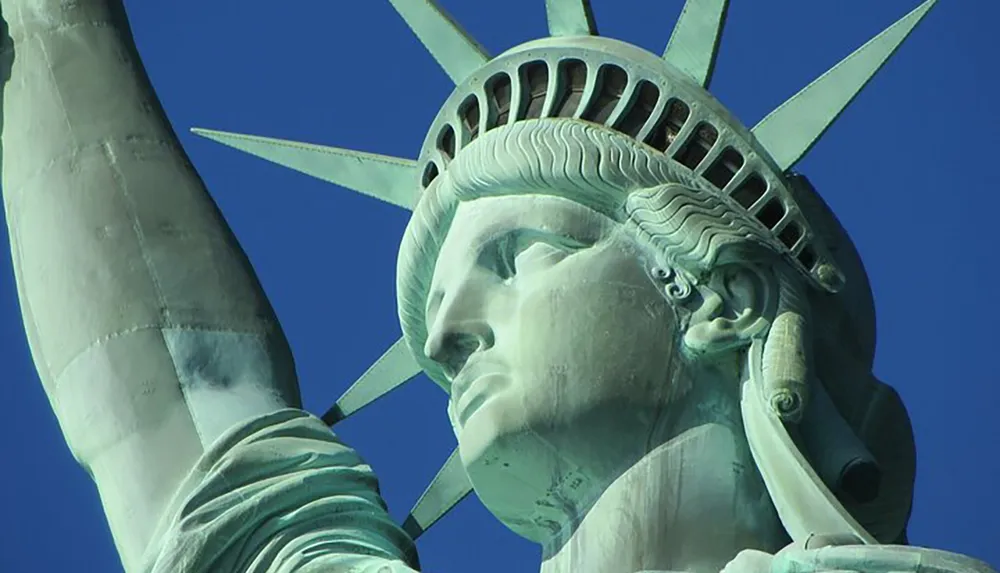 This image presents a close-up view of the iconic Statue of Liberty against a clear blue sky