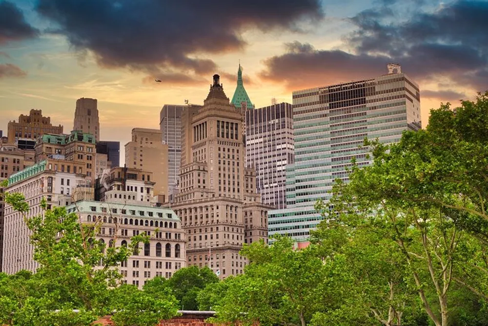 The image depicts a vibrant city skyline at sunset with a foreground of lush green trees and a tapestry of architectural styles against a softly colored sky