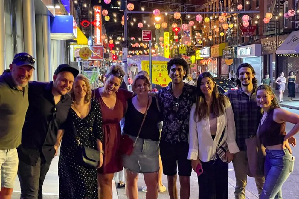 A group of cheerful people poses for a night-time photo on a vibrant street adorned with lanterns