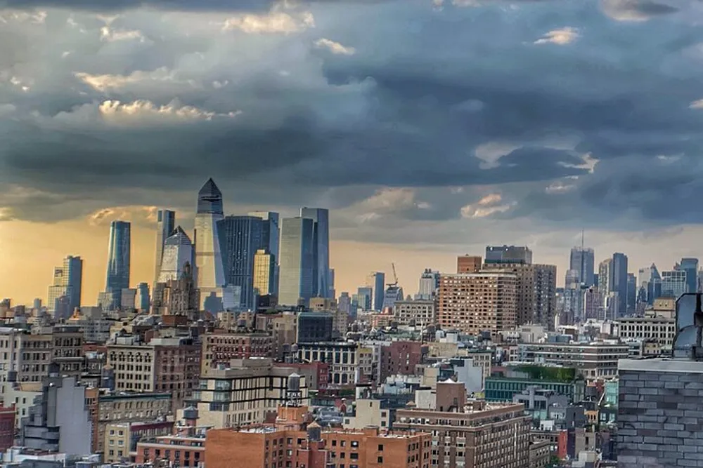 The image shows a cityscape with a mix of modern skyscrapers and older buildings against a dramatic sky with a patchwork of clouds