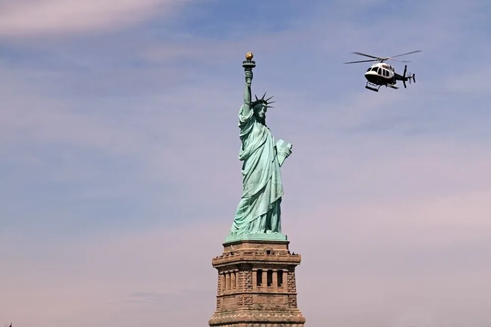 A helicopter flies past the Statue of Liberty under a clear blue sky