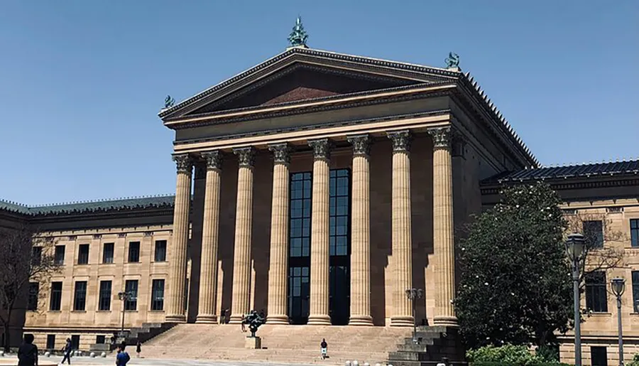 The image shows a large classical building with columns and steps under a clear sky, likely a museum or similar institution.