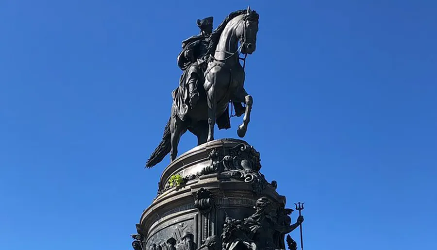 The image shows an equestrian statue of a figure mounted on a rearing horse, set against a clear blue sky.