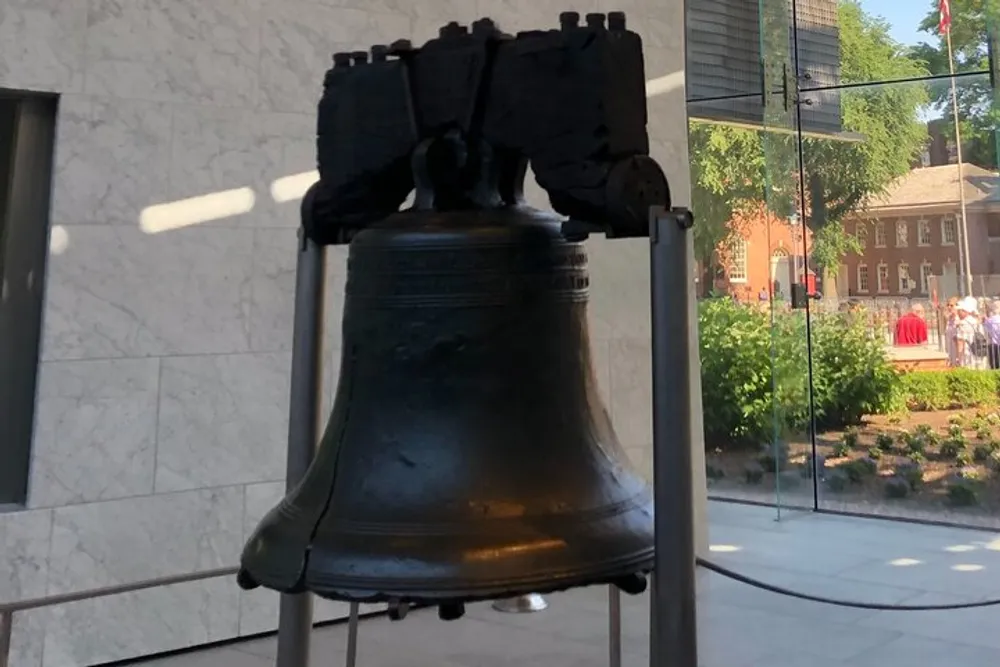 The image shows the Liberty Bell an iconic symbol of American independence displayed in a glass-enclosed pavilion with reflections of the surrounding area