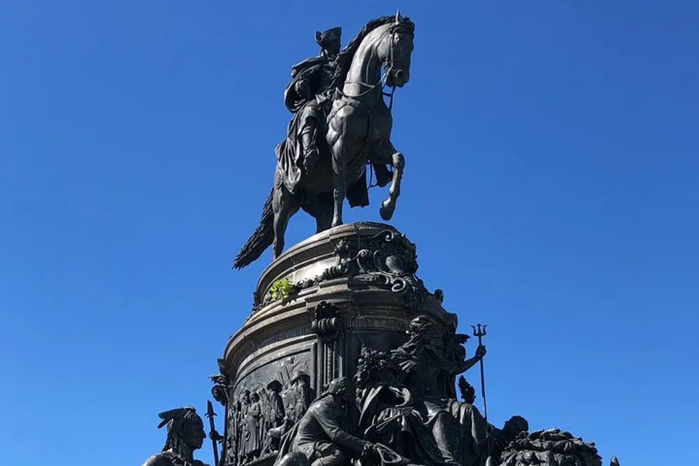 The image showcases an imposing equestrian statue with intricate details set against a clear blue sky