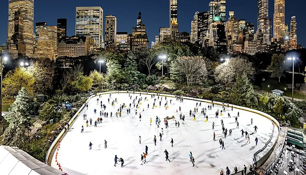 People are ice skating on an outdoor rink at night with a backdrop of illuminated city skyscrapers