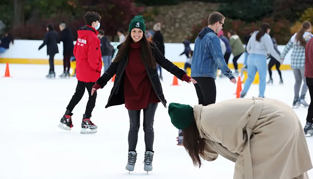 A group of people are enjoying ice skating with a smiling woman in the center balancing herself while another person appears to be bending down or falling in the foreground