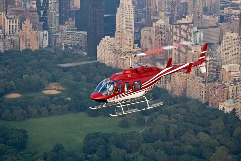 A red helicopter is flying over Central Park with the New York City skyline in the background