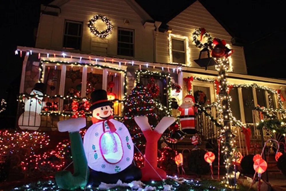 A house is festively decorated with colorful lights inflatable holiday figures wreaths and a Christmas tree creating a vibrant and cheerful nighttime display for the holiday season