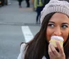 A woman wearing a knitted beanie is smiling as she is about to take a bite from a frosted cupcake outdoors