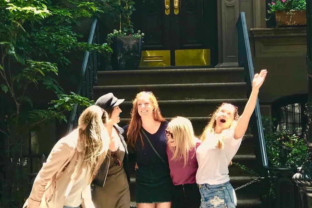 A group of happy young women are standing in front of a residential doorway sharing a joyful moment together