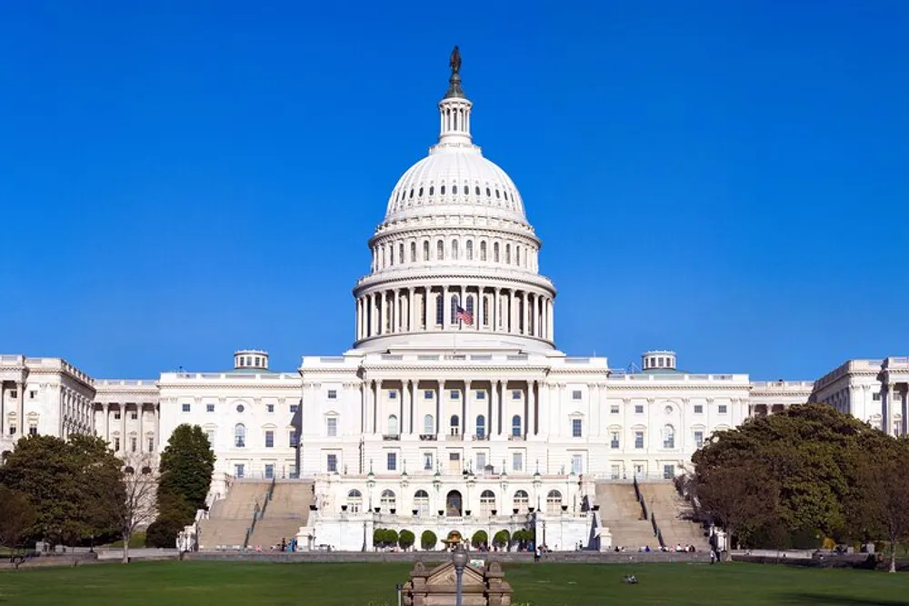 The image shows the United States Capitol building a symbol of the American government with its iconic dome and expansive front lawn under a clear blue sky