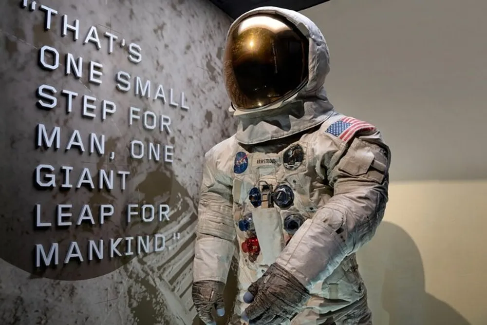 This image features a life-size model or mannequin of an astronaut in a vintage NASA spacesuit displayed in front of a wall with the famous quote Thats one small step for man one giant leap for mankind