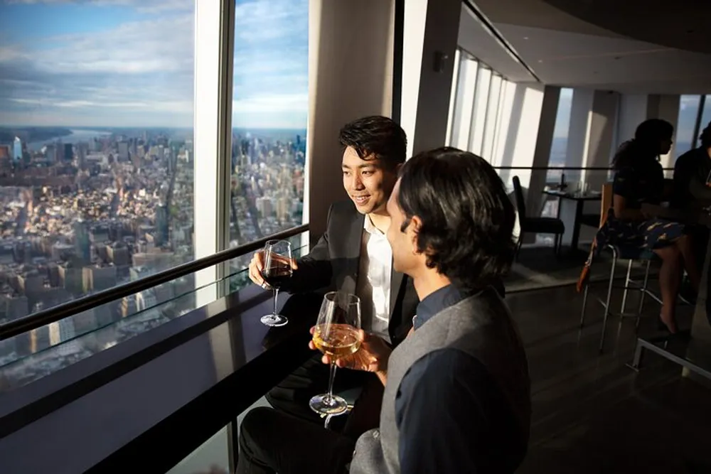 Two people are enjoying drinks and a conversation with a panoramic city view from a high-rise building