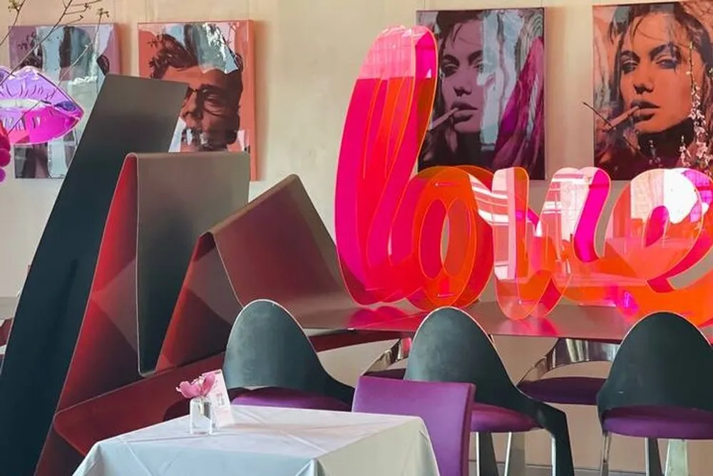 The image shows a modern and artistically decorated interior of a cafe or restaurant with vibrant sculptures and artwork featuring bold representations of the word love and stylized portraits