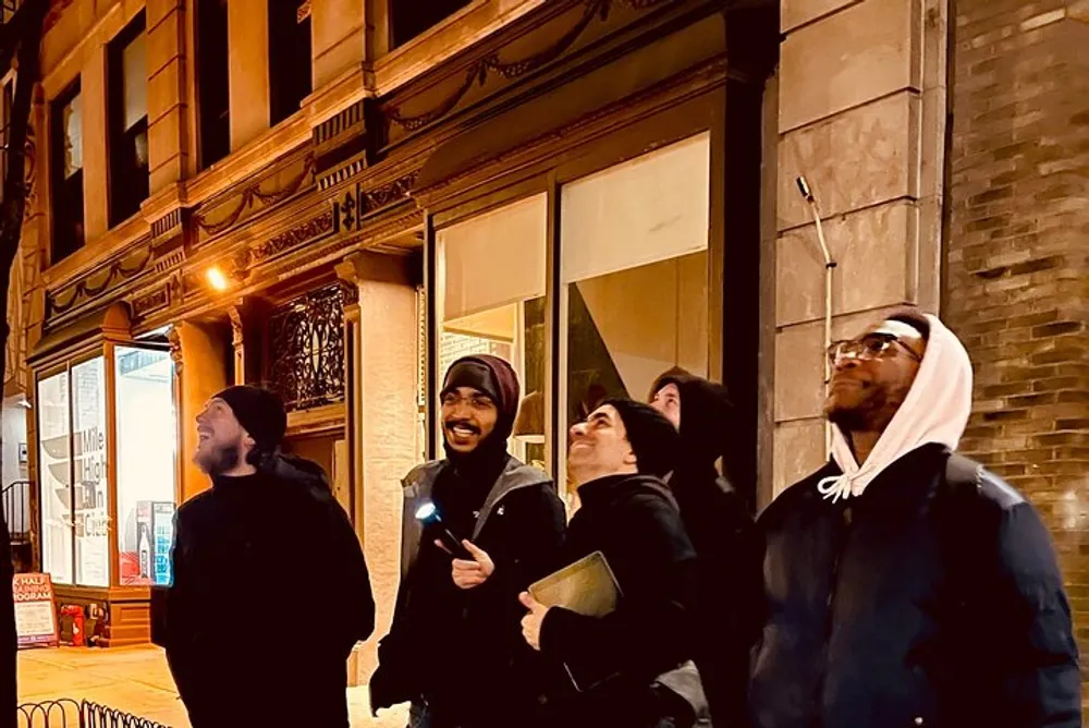 Four people are looking upwards with various expressions of interest or amusement on a city street at night