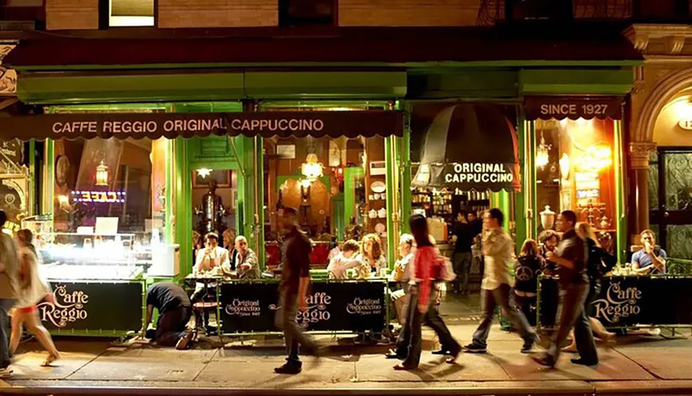 The image depicts a bustling street scene at night outside the Caffe Reggio with people dining al fresco and pedestrians walking by