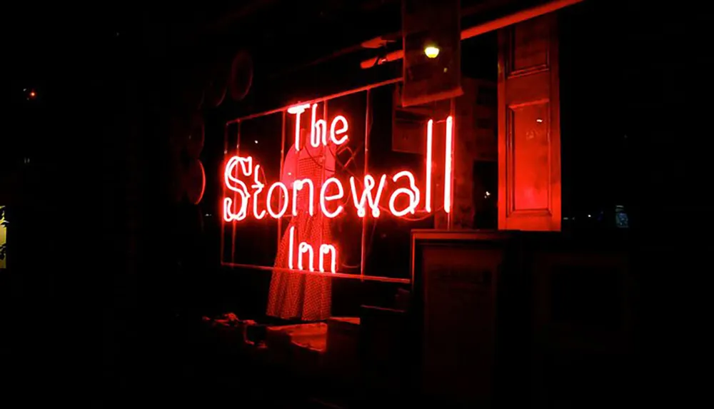 The image shows the neon sign of The Stonewall Inn a notable landmark associated with LGBTQ rights glowing in red against the night