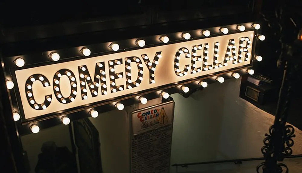 The image shows an illuminated sign that reads COMEDY CELLAR with bright light bulbs around the border