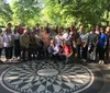 A group of people is gathered around the Imagine mosaic memorial in Central Park likely tourists or fans paying tribute