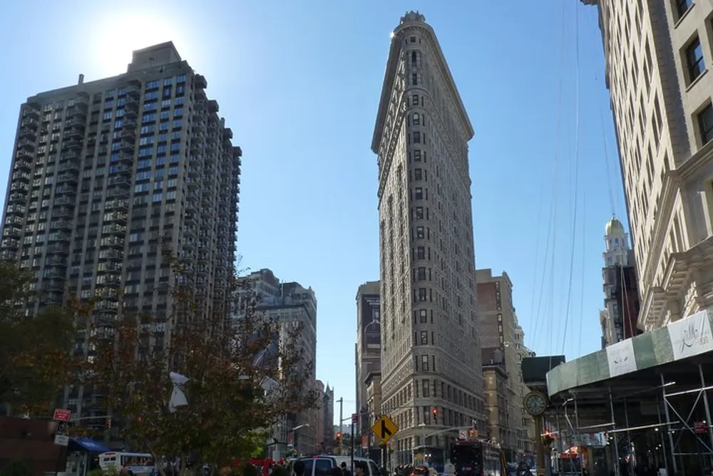 The image captures a sunny day view of the iconic Flatiron Building a triangular skyscraper amidst other buildings under a blue sky