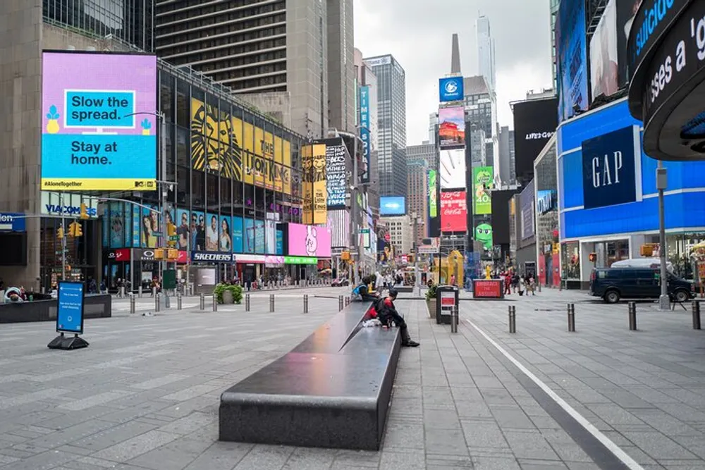 The image shows an unusually empty Times Square with electronic billboards displaying public health messages including one that reads Slow the spread Stay at home