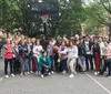 A diverse group of people are posing for a photo on a basketball court with urban surroundings