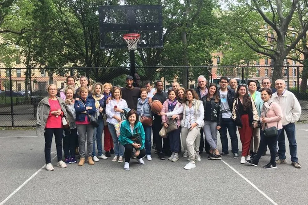 A diverse group of people are posing for a photo on a basketball court with urban surroundings
