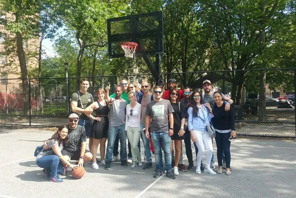 A diverse group of people are posing for a photo on an outdoor basketball court with one person holding a basketball