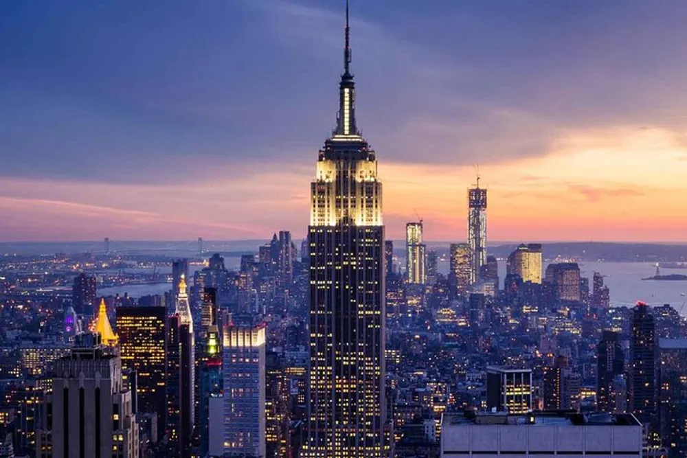 This image captures a breathtaking evening view of the New York City skyline with the Empire State Building prominently illuminated against a twilight sky