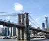 The image shows the Brooklyn Bridge spanning across the East River with the Manhattan skyline in the background on a clear day