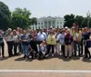 A group of tourists is posing for a photo in front of the White House on a sunny day