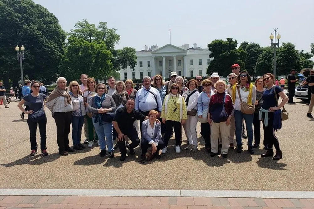 A group of tourists is posing for a photo in front of the White House on a sunny day