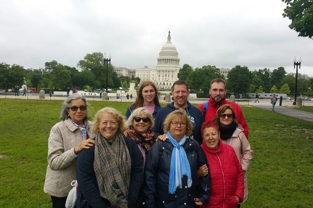 A group of smiling people poses for a photo in front of the United States Capitol building on a cloudy day
