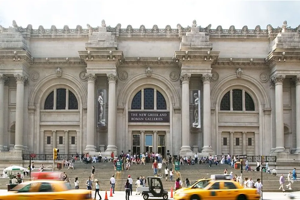 This is a busy day outside the entrance of the Metropolitan Museum of Art in New York City highlighted by bustling pedestrians and classic yellow taxis