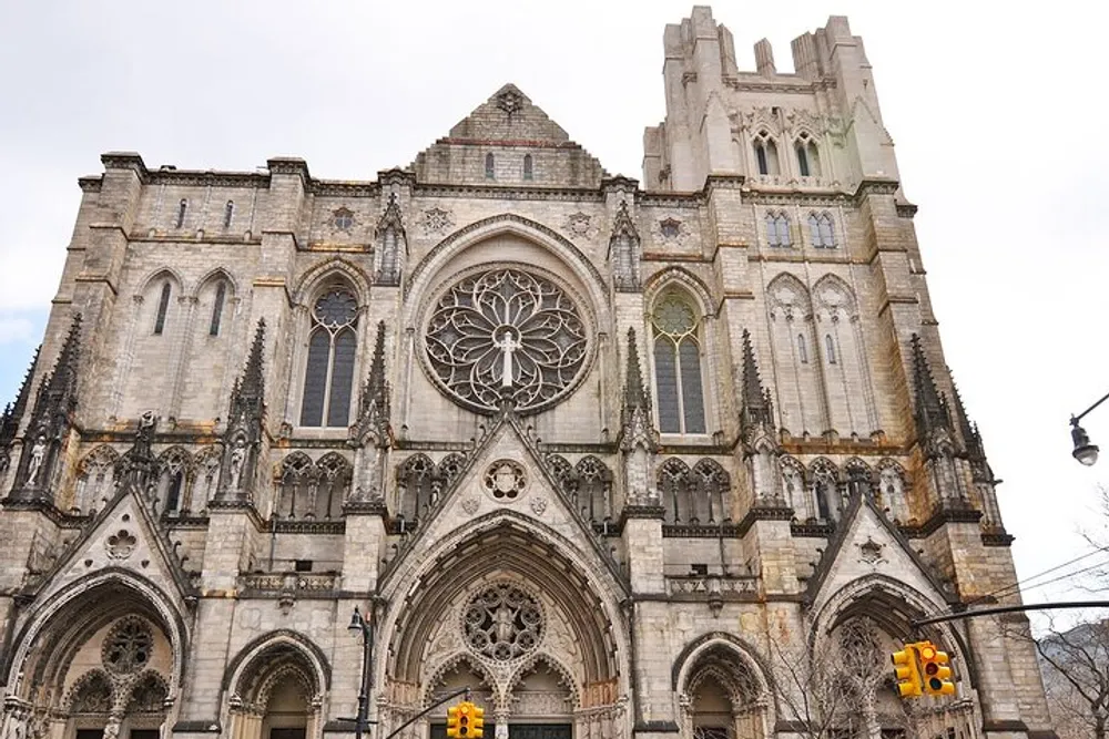 The image shows the ornate facade of a Gothic-style cathedral featuring a large rose window and intricately carved stonework with traffic lights visible at the street level