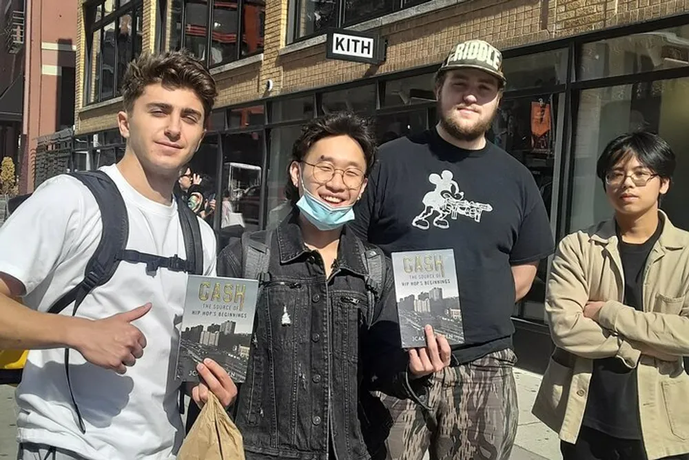 Four individuals are posing for a photo on a sunny day with two of them holding copies of a book titled CASH with a cityscape on the cover